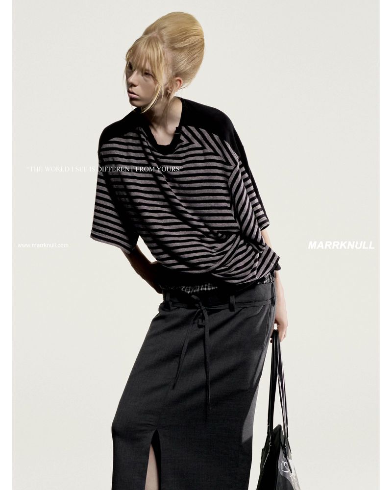 Model with a high bouffant blonde hairstyle wearing a striped top and dark skirt against a white studio background.