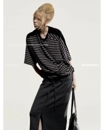 Model with a high bouffant blonde hairstyle wearing a striped top and dark skirt against a white studio background.