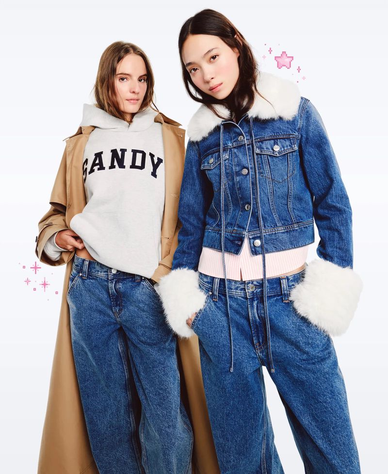 Two fashion models in stylish denim and hoodies pose in a bright studio. One wears a tan trench coat. Fashionable and modern.