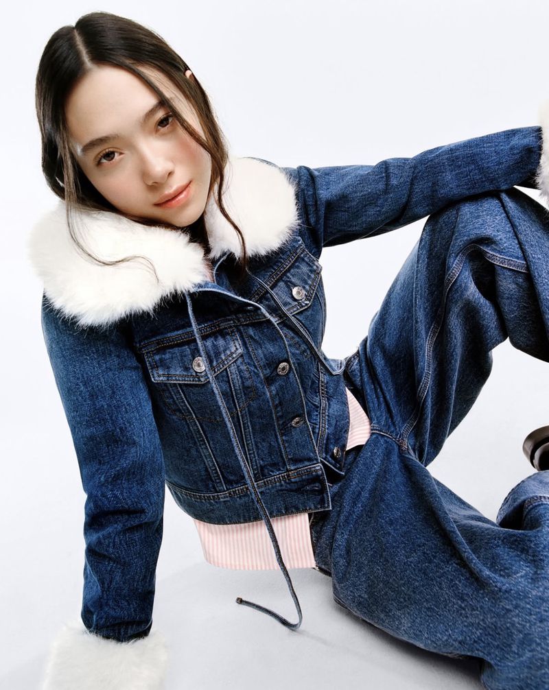 A young woman poses in a cropped denim jacket with a white fur collar and matching wide-leg jeans against a plain white backdrop.