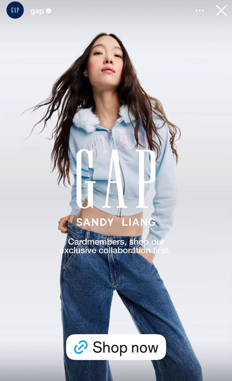 Asian female model poses wearing a light blue Gap sweatshirt and jeans against a neutral studio backdrop for a fashion campaign.