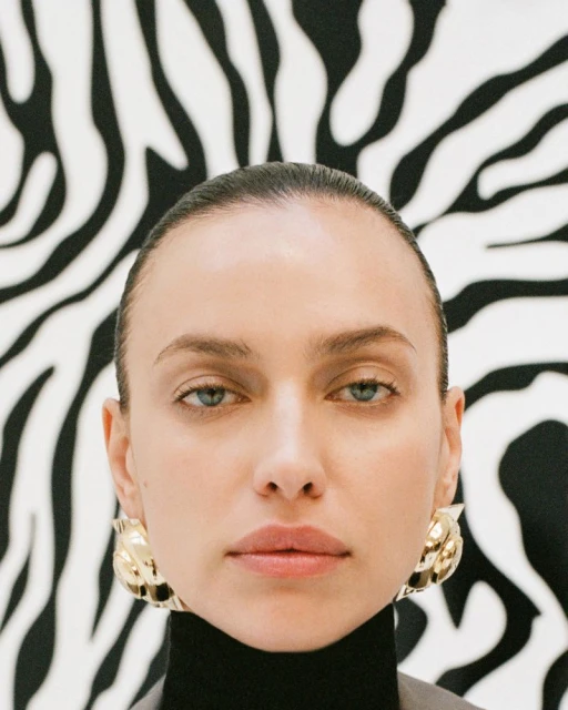 Close-up portrait of a woman with golden earrings against a black and white zebra-print background. Beauty and fashion concept.