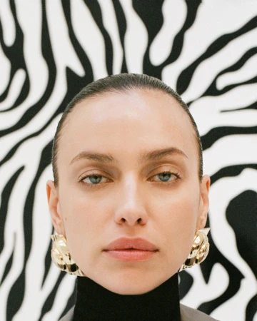 Close-up portrait of a woman with golden earrings against a black and white zebra-print background. Beauty and fashion concept.