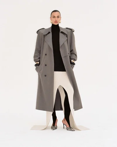 Model Irina Shayk wearing an oversized grey trench coat and black turtleneck against a white studio background.