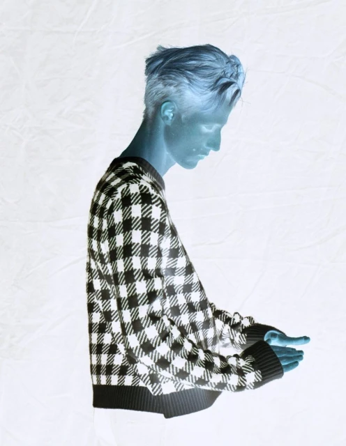 Studio shot of a blue-toned young adult male in a black-and-white checkered sweater against a white textured backdrop.