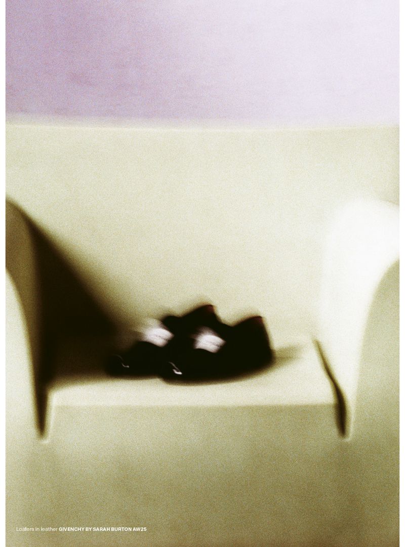 Close-up studio shot of black leather shoes with buttoned straps on a shelf with soft lighting and a pastel background.