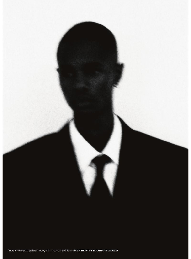Portrait of an adult male in a black suit and tie against a white background in a studio setting. The image is slightly blurred.
