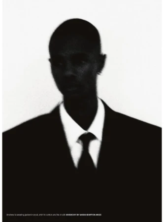 Portrait of an adult male in a black suit and tie against a white background in a studio setting. The image is slightly blurred.