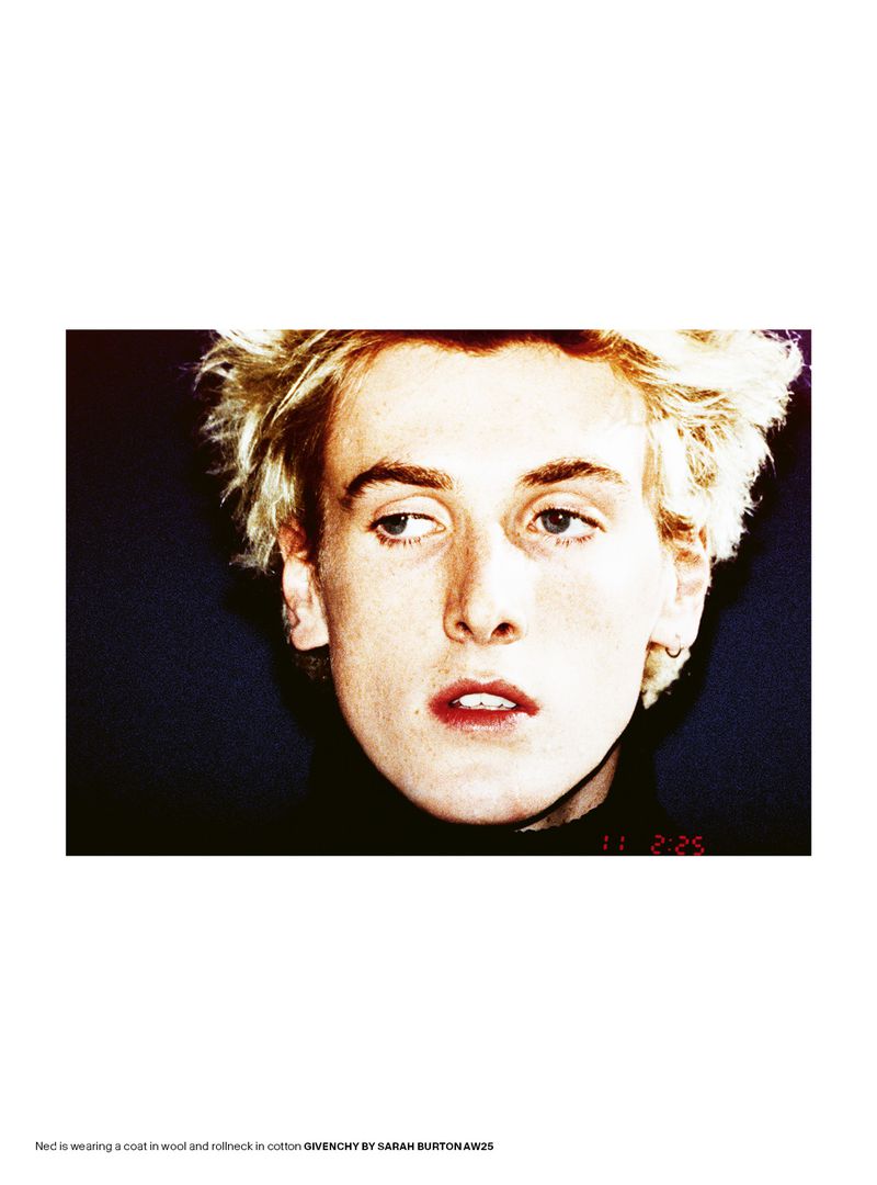 Close-up portrait of a young man with blonde hair and red lips against a dark background in an editorial magazine style.