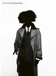 Model with an afro silhouette wearing an overcoat, tailored suit jacket, shirt, and tie against a pure white background.