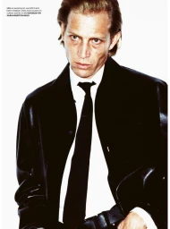 Man wearing a dark jacket, white shirt, and black tie against a bright white background for an editorial spread.