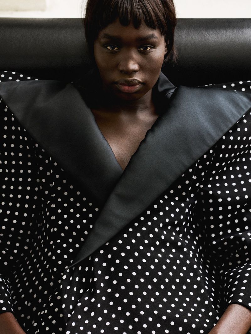 Close-up of a dark-skinned woman in a polka dot top with a large black collar, looking directly at the camera in a studio setting.