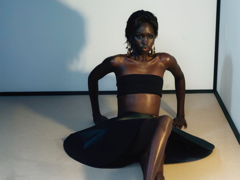 Portrait of a striking African woman with short black hair and gold earrings in a black strapless top and skirt, sitting indoors.