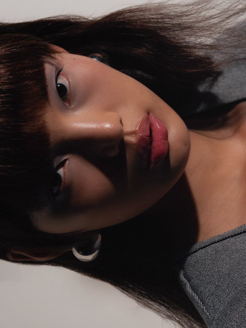 Portrait of a brunette woman with bangs looking at the camera, face partially shadowed, wearing a grey top. Beauty and fashion.