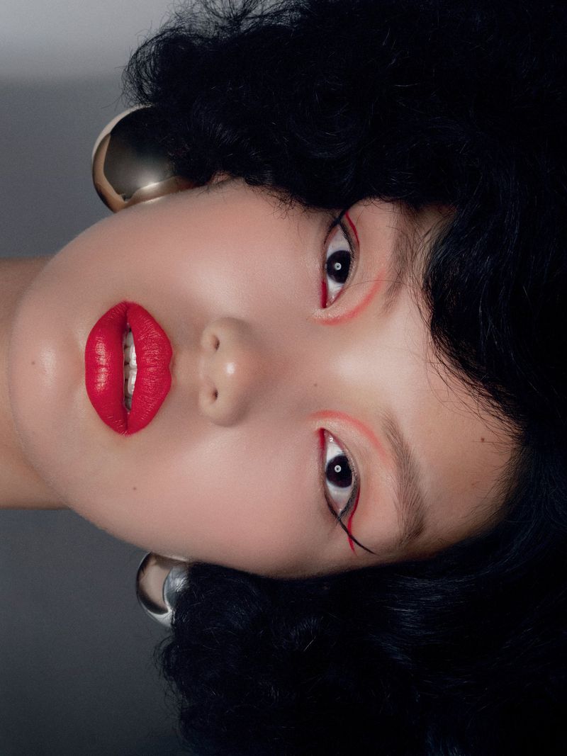 Close-up portrait of a stylish adult female with bold red lipstick, black curly hair, and wearing large, silver hoop earrings.