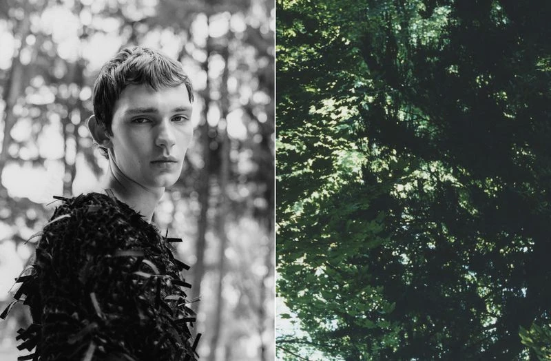 Portrait of a young man with dark hair wearing a textured top, set against a blurred forest background and foliage.