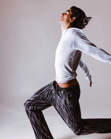 Man wearing a white long-sleeve shirt and zebra print pants posing in profile against a seamless light grey background.