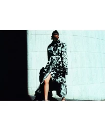 Model Betsy Gaghan wears a black and white mottled coat posing against a curved tiled wall in high-contrast light.