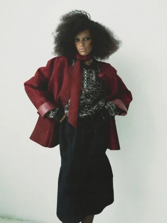 Model Kukua Williams wearing a red jacket and dark skirt against a plain white studio background.