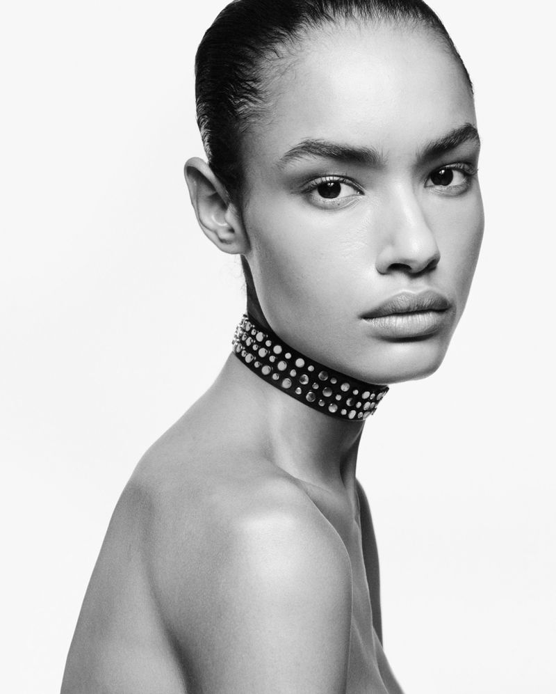 Monochrome close-up portrait of model Ana Beatriz Cortes wearing a studded choker necklace against a bright white background.