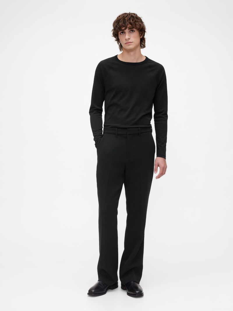 Full shot of an adult male fashion model posing in black long-sleeve shirt and black trousers on a white studio background.