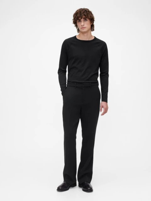 Full shot of an adult male fashion model posing in black long-sleeve shirt and black trousers on a white studio background.