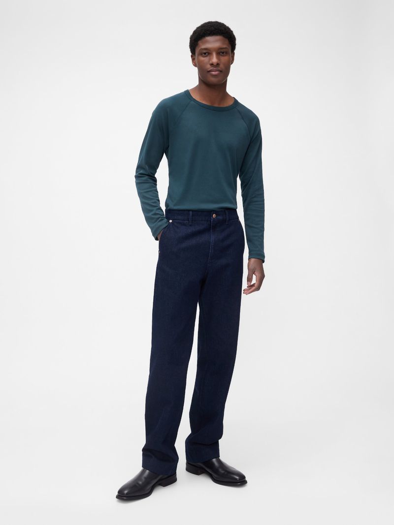 Full shot of a black male model in a teal long-sleeved shirt and navy dress pants standing against a white backdrop in a studio.