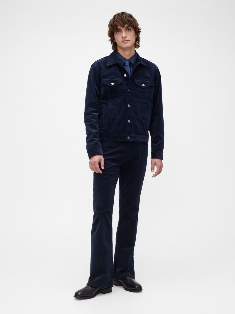 Full-length studio shot of an adult male model in a dark blue corduroy jacket, pants, and black leather shoes on a white backdrop.