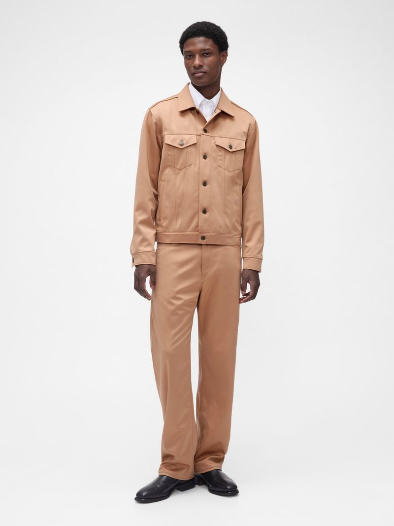 Full-length portrait of a Black male model wearing a matching tan jacket and trousers on a solid white background in a studio.