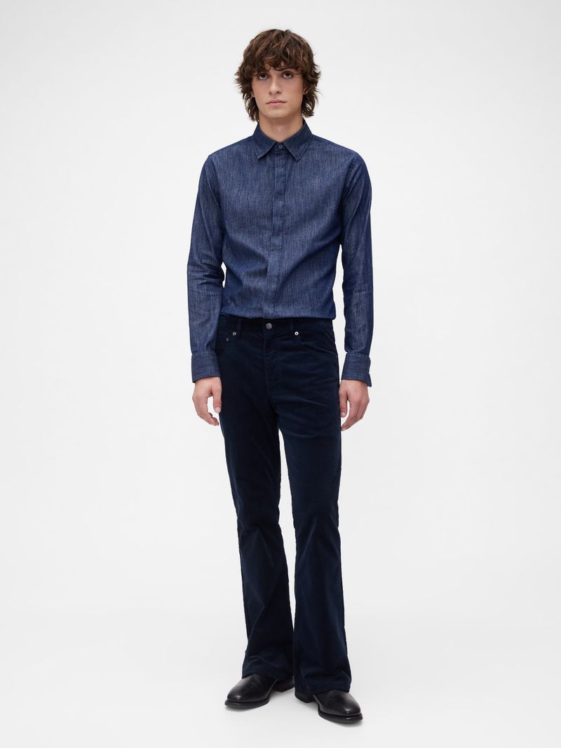 Full-length shot of an adult male posing in a blue button-down shirt, navy corduroy pants, and black leather shoes on a white backdrop.