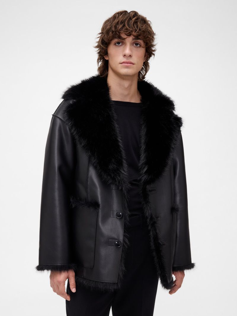 Male model in a black leather coat with a plush black shearling collar against a neutral studio backdrop.