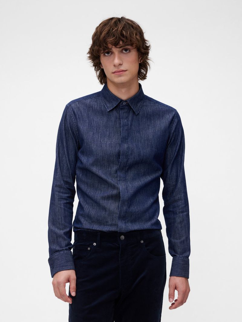 Model wearing a dark blue denim button-up shirt and dark trousers against a white seamless studio backdrop.