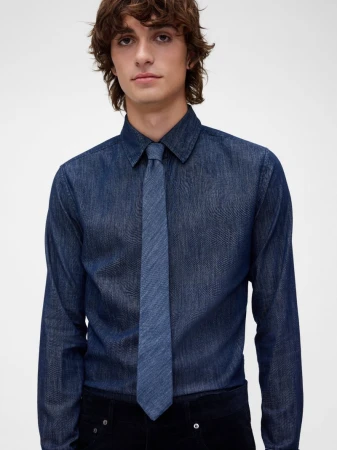 Young male model wearing a dark denim button-down shirt and matching tie against a seamless white background.
