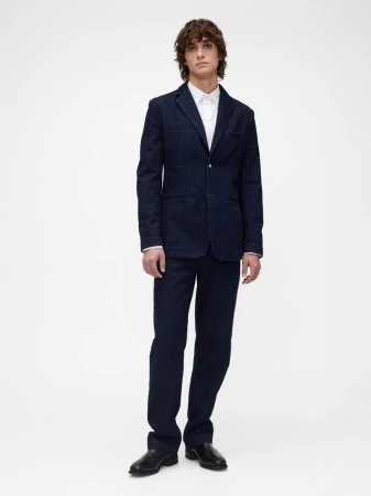 Full-length portrait of a male model wearing a dark navy suit and white shirt against a seamless white background.