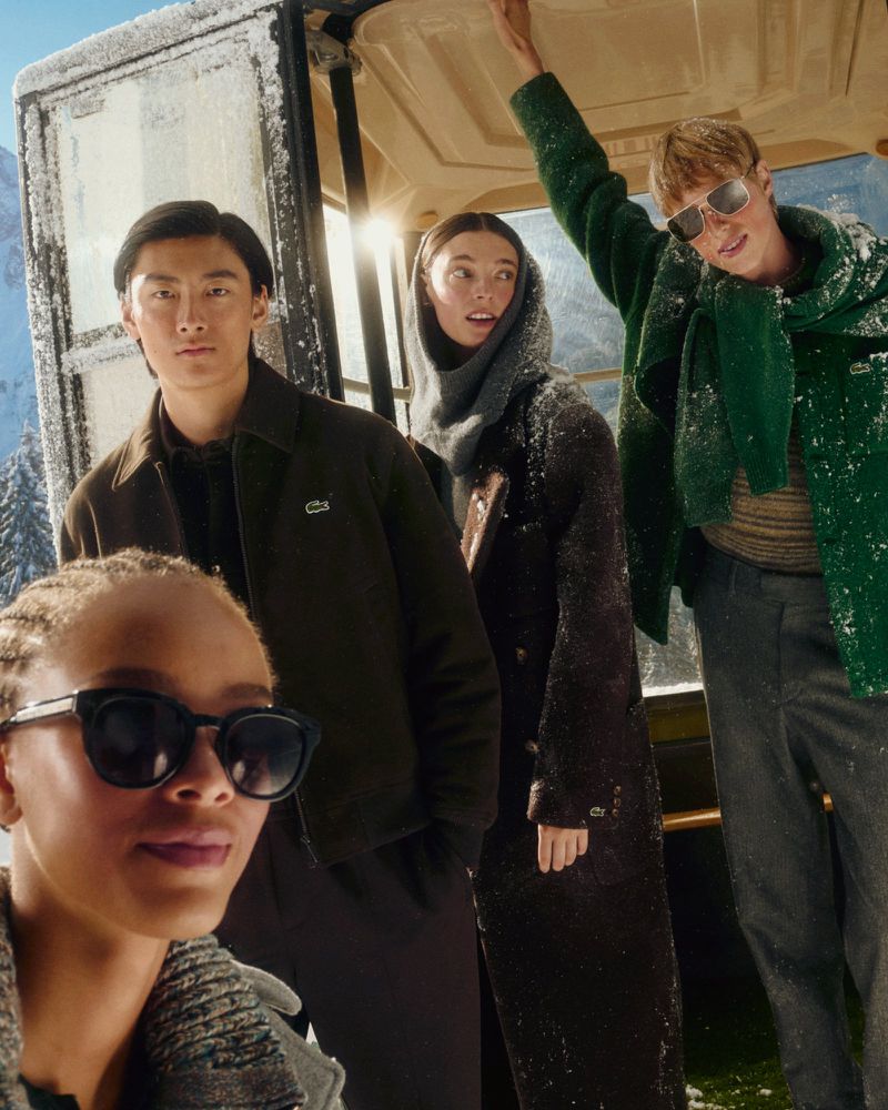 Group of four people inside an open-top vehicle wearing coats and scarves in a snowy, mountainous landscape, with bright, soft lighting.