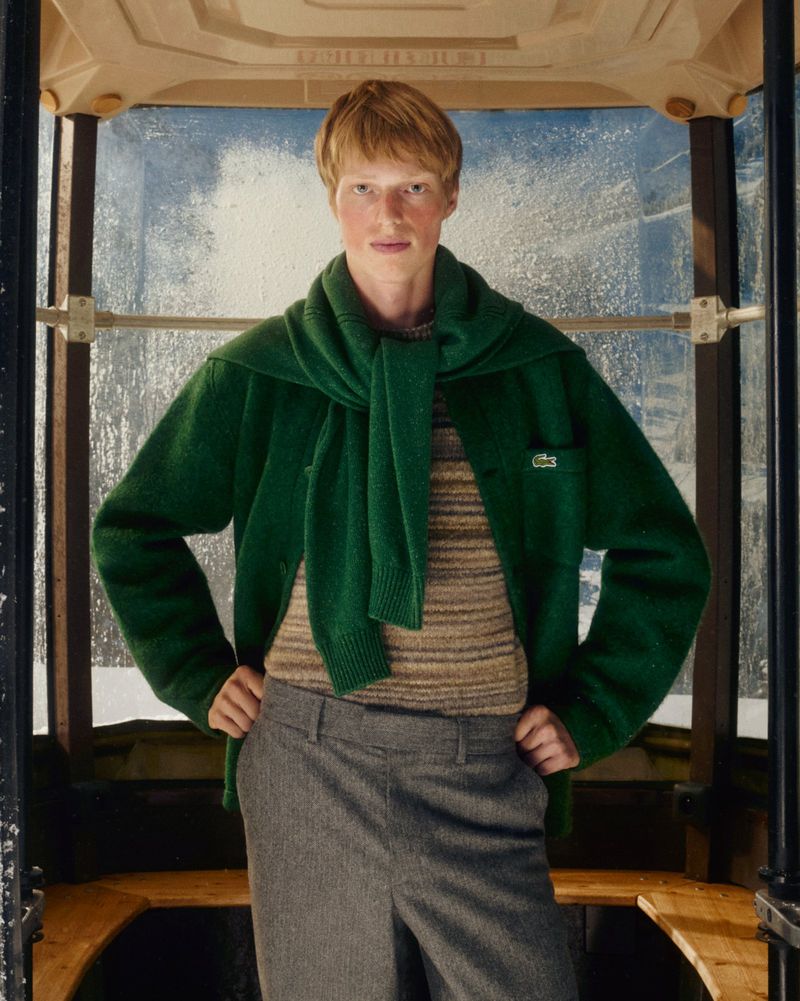 Young adult poses in a vintage cable car wearing a green jacket and grey pants, embodying classic style in a unique setting.