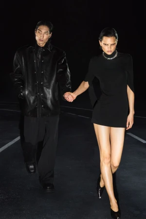 Two fashion models holding hands while walking on a dark road wearing all-black outfits for Alexander Wang.