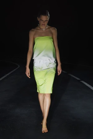 Model walking on a dark road wearing a gradient lime green strapless top and skirt with a silver necklace.