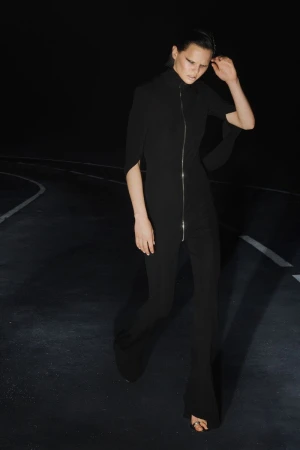 Model wearing a black zip-up jumpsuit walking along a dark asphalt road at night for Alexander Wang Resort 2026