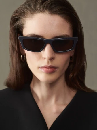 Portrait of a woman with sunglasses wearing a black top, set against a neutral gray background in a studio setting. Fashionable and sleek.