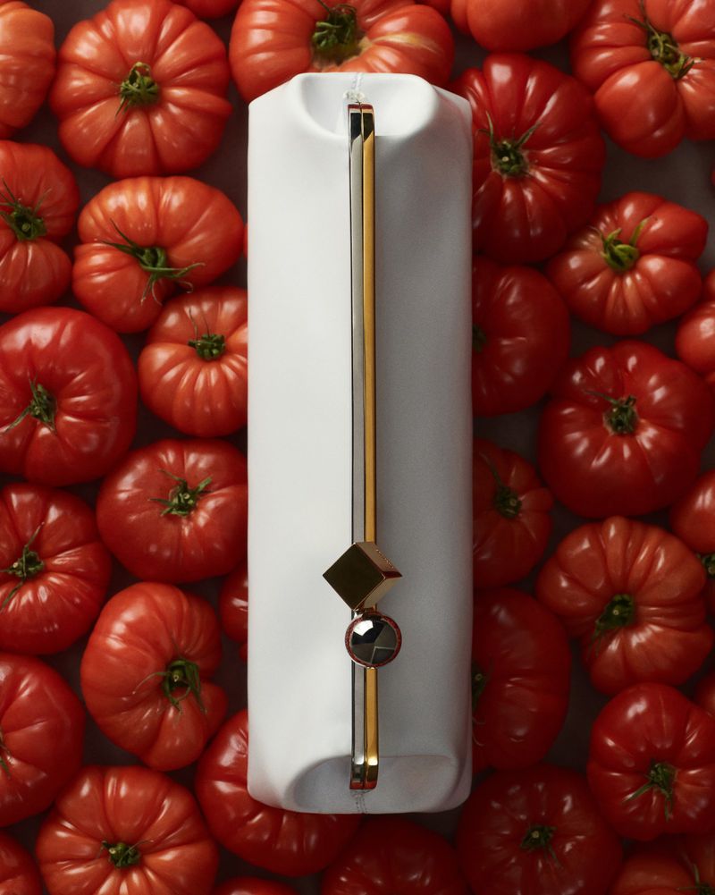 A white purse with a gold handle and hardware is surrounded by red tomatoes creating a visually striking product still life.