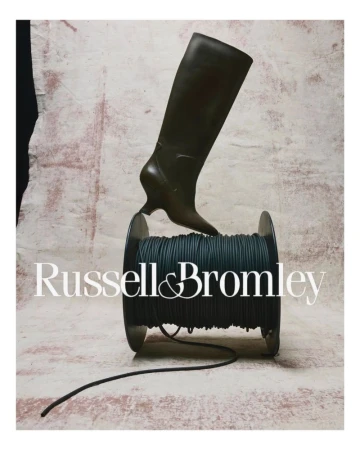A tall dark leather boot is staged upright atop a spool of dark cord, with the Russell & Bromley logo in the foreground.