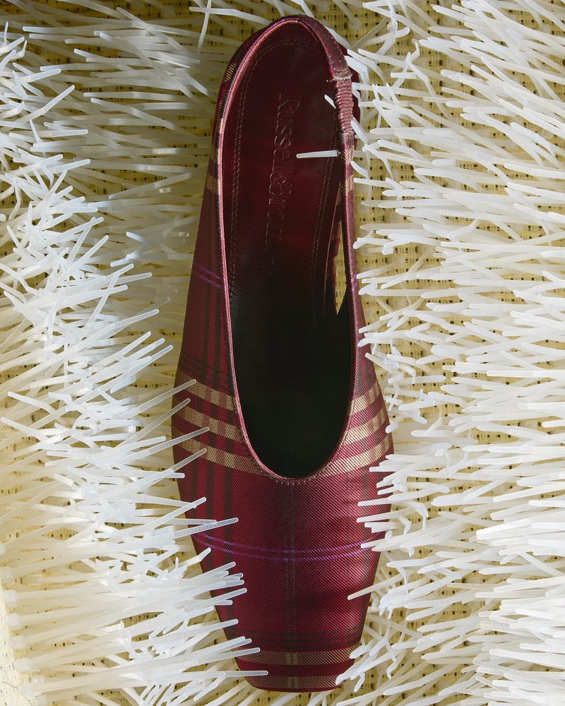 Burgundy and gold women's slingback heel shoe sits atop a bed of thin, pale yellow and white paper grass-like filler.