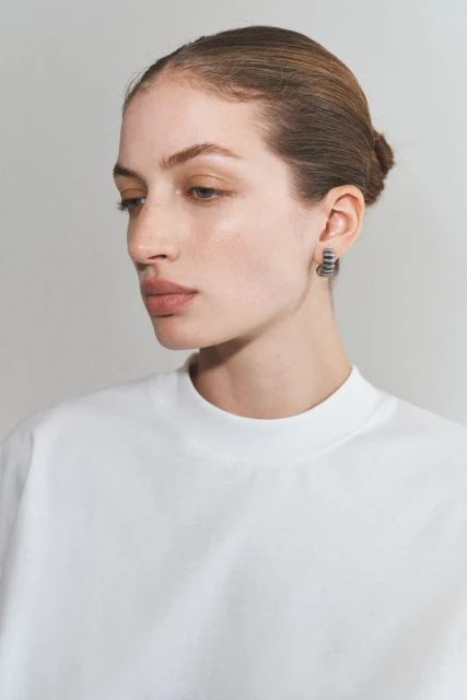 Close-up portrait of an adult woman with neutral expression wearing a white top and hoop earrings against a neutral backdrop.