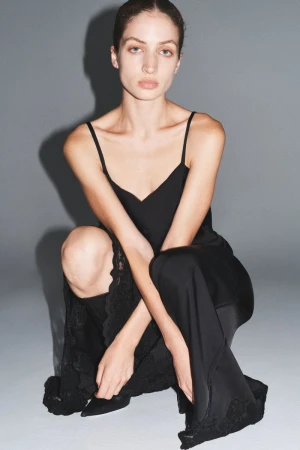 Elegant adult woman in a black slip dress posing in a photo studio. The dress has lace trim. She is sitting on the floor.