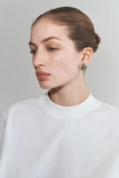 Model with pulled back hair wearing a white top and small hoop earrings against a neutral background