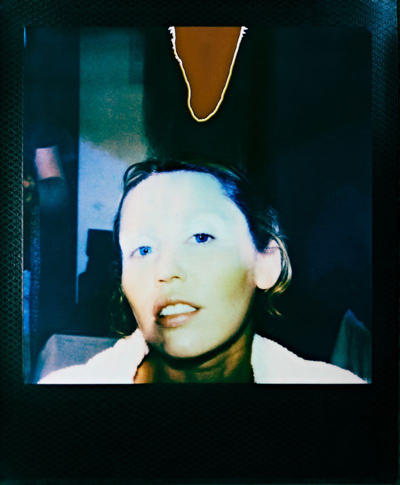 Portrait of an adult female with a white towel around her shoulders in front of a dark background with a brown, abstract shape.
