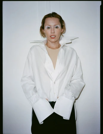 Miley Cyrus wearing an oversized white button-down shirt and black trousers against a plain white background.