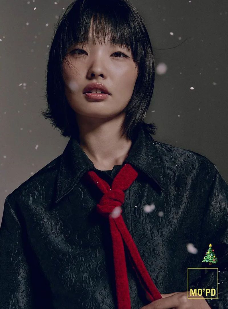 Portrait of a young Asian woman with dark hair and a red scarf-like tie, looking directly at the camera with snow effects and blurred backdrop.