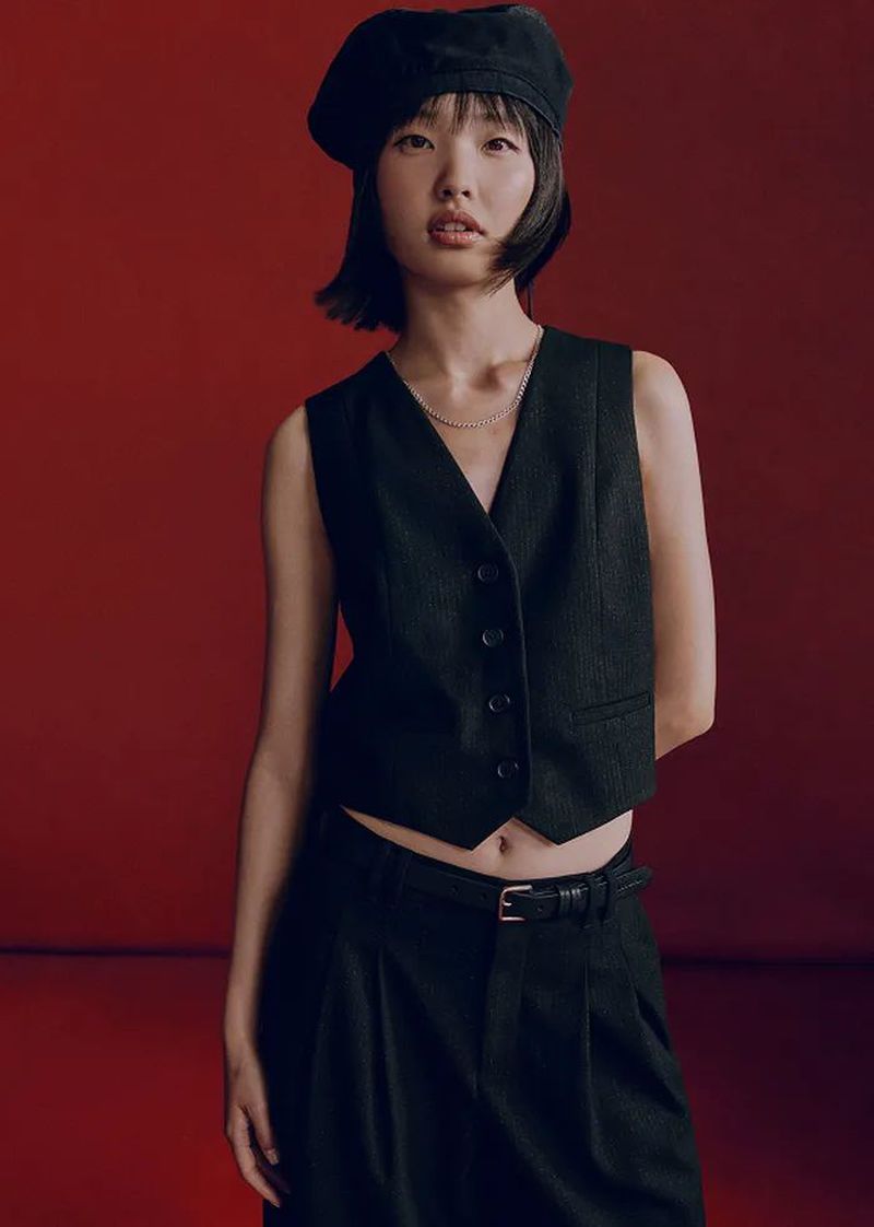 Portrait of an Asian woman wearing a beret, black vest and pants against a red background in a fashion style look.
